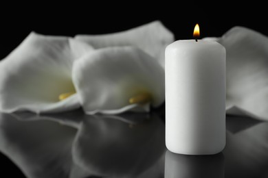 Burning candle and white calla lily flowers on black mirror surface in darkness, closeup with space for text. Funeral symbol