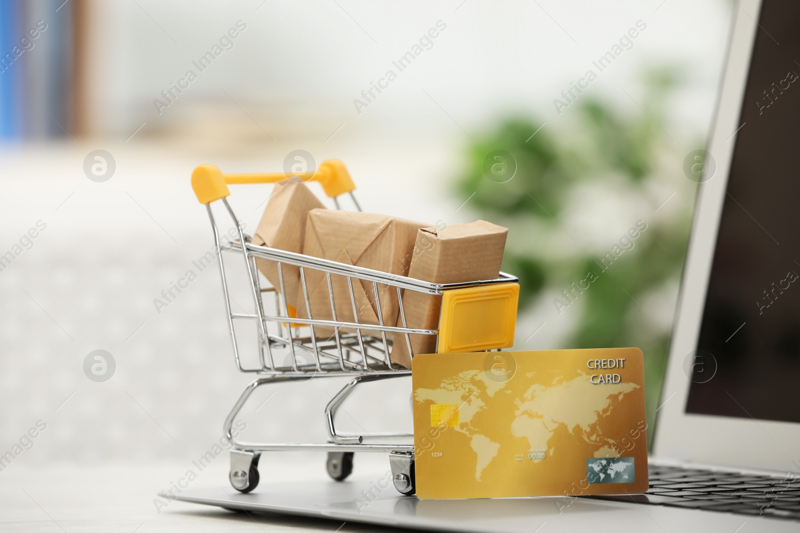 Photo of Online payment concept. Small shopping cart with bank card, boxes and laptop on table