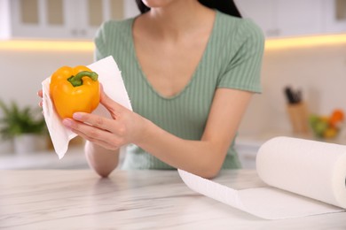 Photo of Woman wiping bell pepper with paper towel in kitchen, closeup