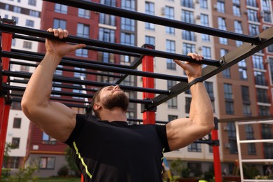 Photo of Young man training on monkey bars at outdoor gym