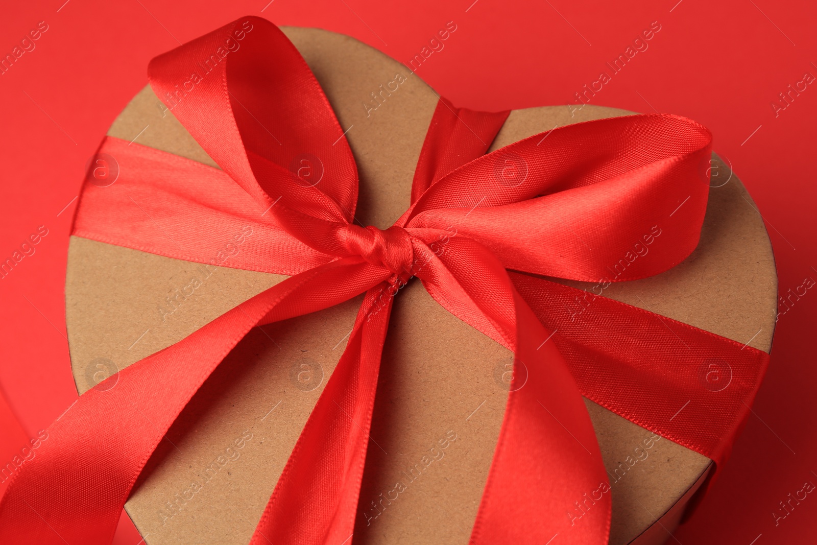 Photo of Beautiful heart shaped gift box with bow on red background, closeup