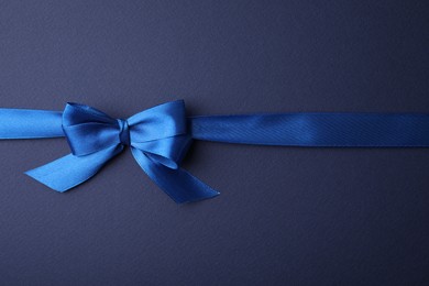 Photo of Bright satin ribbon with bow on blue background, top view