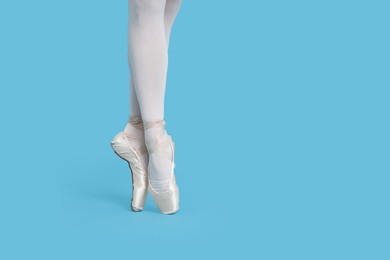 Young ballerina in pointe shoes practicing dance moves on light blue background, closeup. Space for text