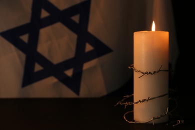 Photo of Barbed wire and burning candle on black background. Holocaust memory day