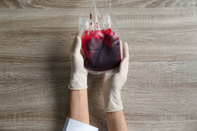 Photo of Woman holding blood for transfusion at wooden table, top view. Donation concept