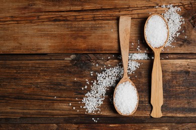 Photo of Spoons with natural sea salt on wooden table, flat lay. Space for text