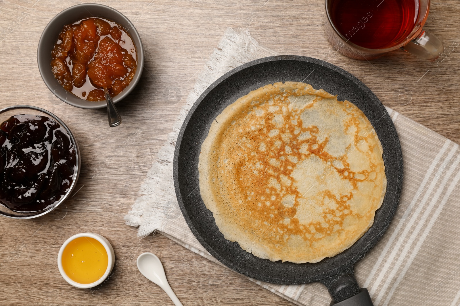 Photo of Frying pan with delicious crepe, jams, honey and aromatic tea on wooden table, flat lay
