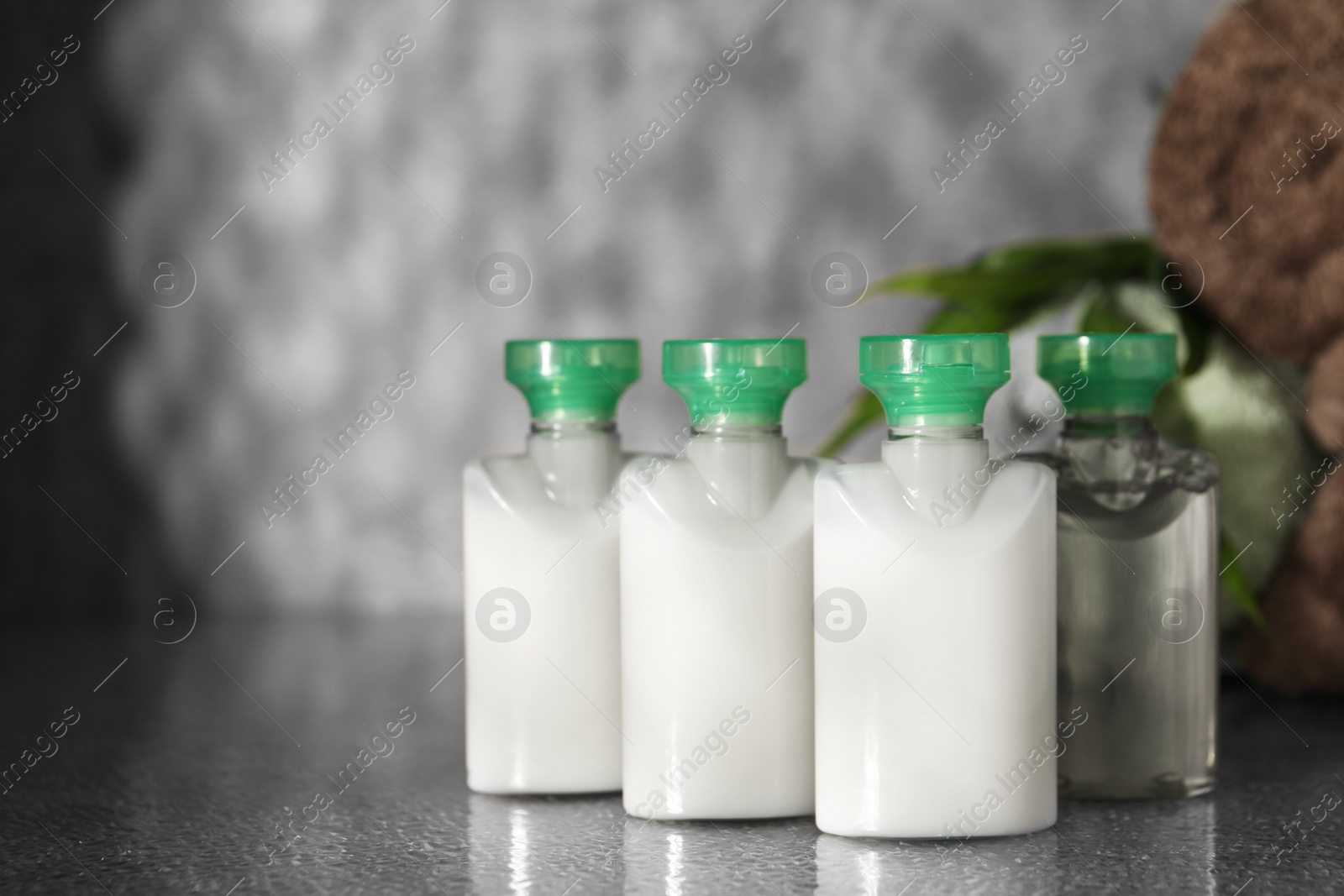 Photo of Mini bottles of cosmetic products on grey textured table, space for text