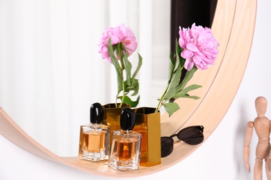 Photo of Stylish round mirror with sunglasses, perfume and flower on white wall indoors. Interior design