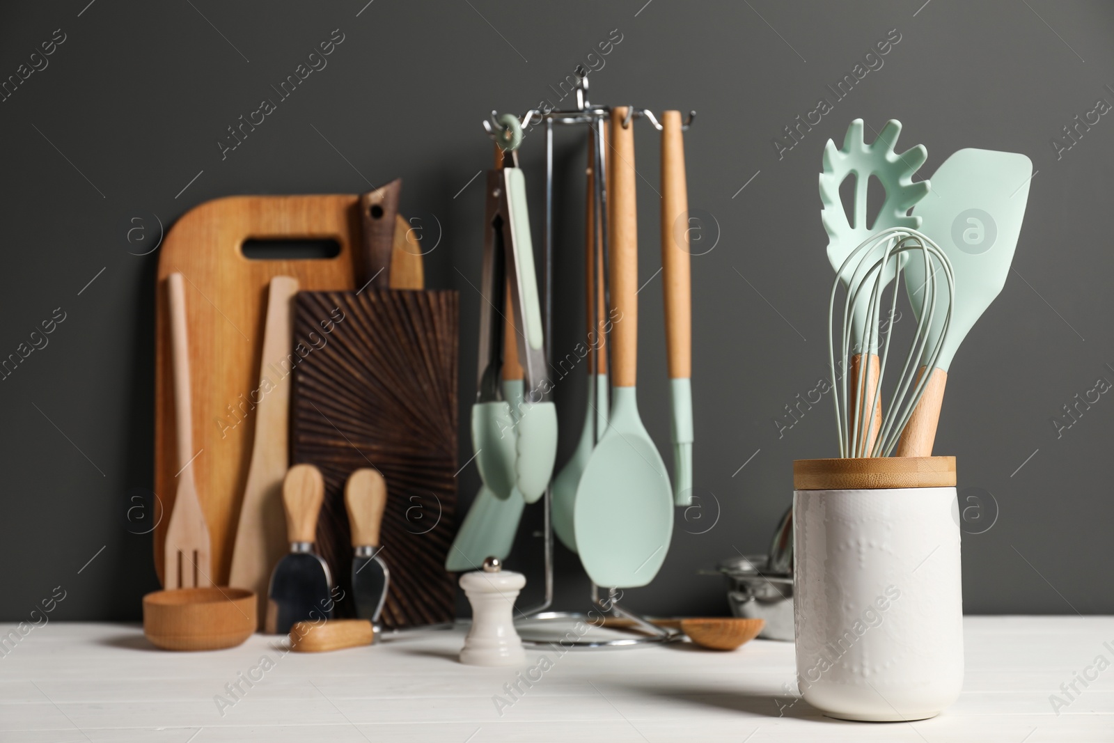 Photo of Set of different kitchen utensils on white wooden table against grey background