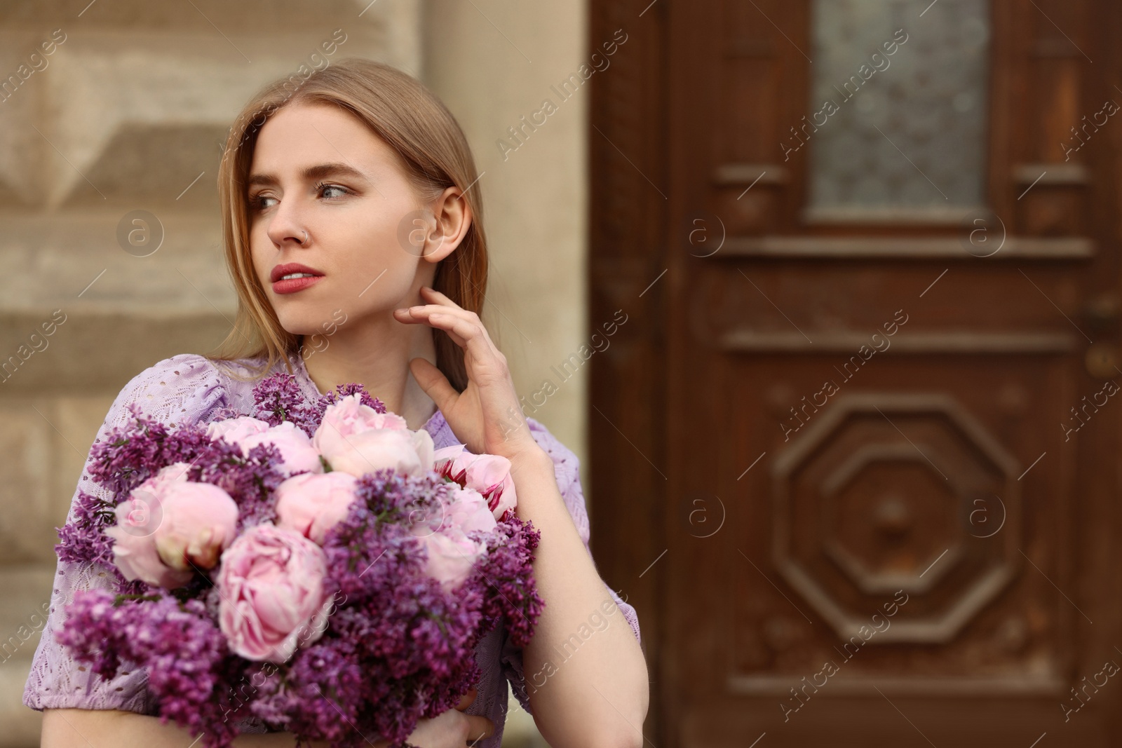 Photo of Beautiful woman with bouquet of spring flowers near building outdoors, space for text