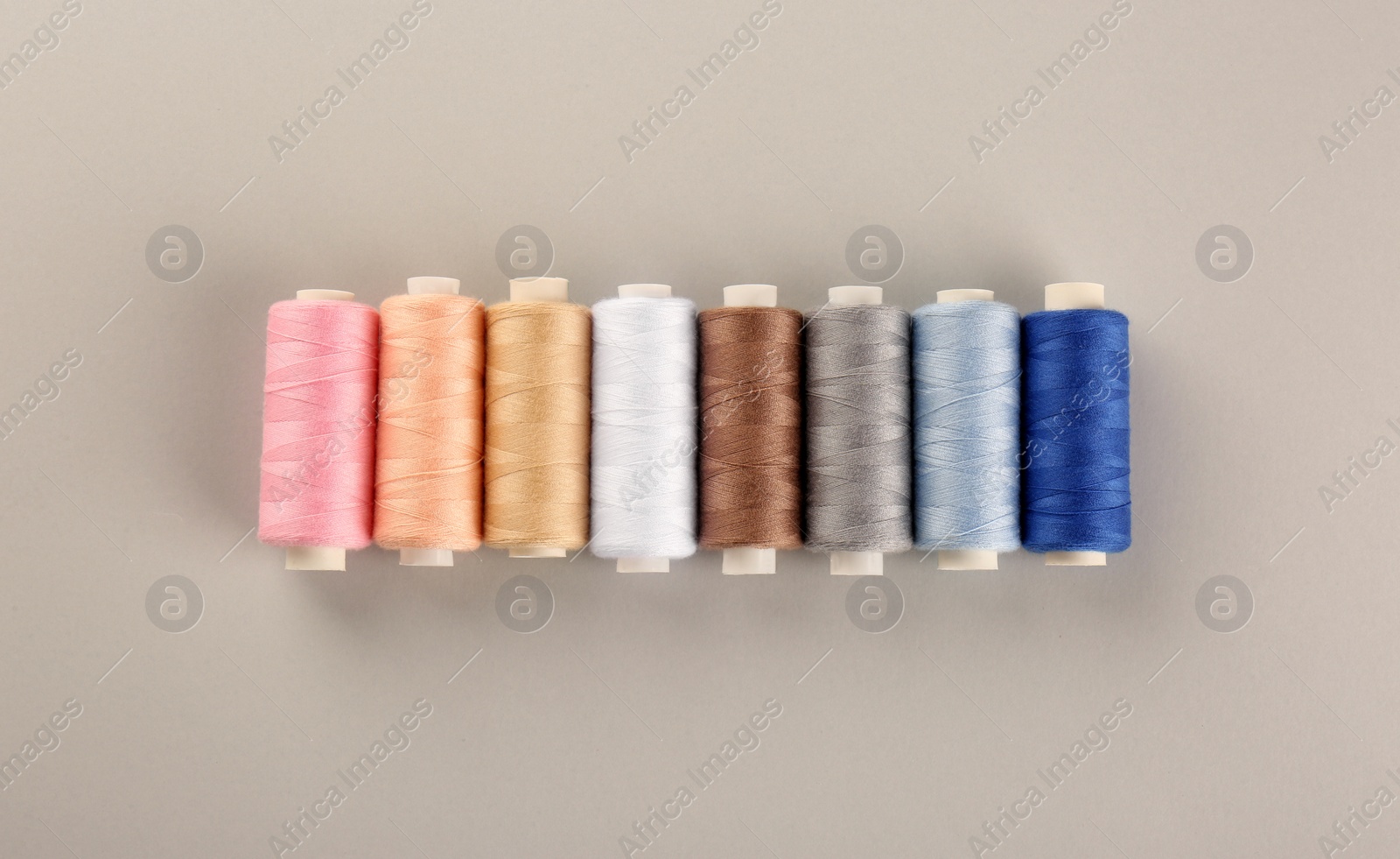 Photo of Different colorful sewing threads on light grey background, flat lay