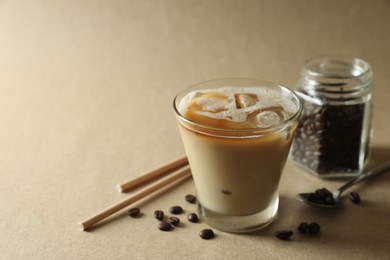 Photo of Refreshing iced coffee with milk in glass, straws and beans on beige background, closeup. Space for text