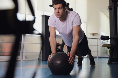 Photo of Athletic man doing plank exercise with medicine ball in modern gym