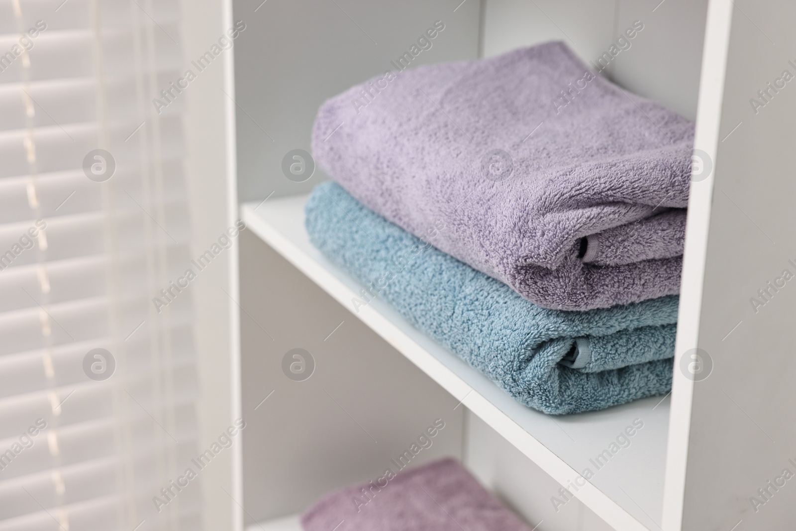 Photo of Stacked fesh towels on shelf indoors. Space for text