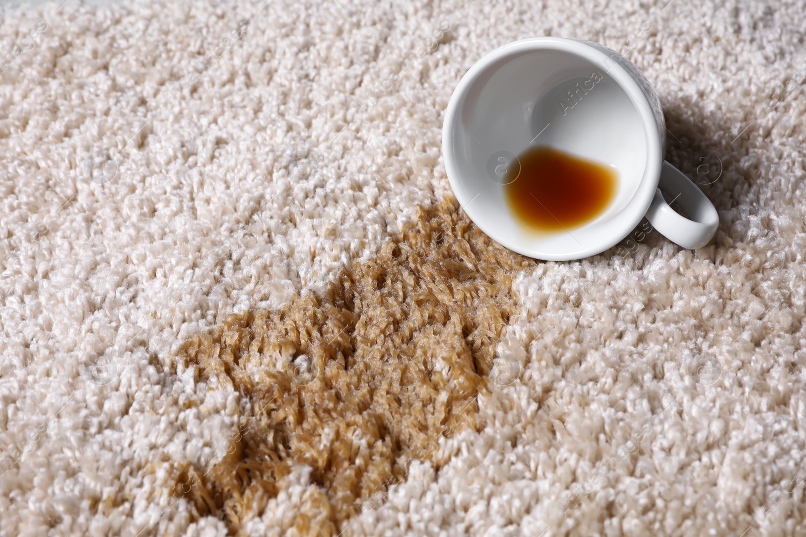 Photo of Overturned cup and spilled tea on beige carpet, closeup