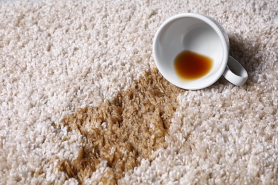 Photo of Overturned cup and spilled tea on beige carpet, closeup