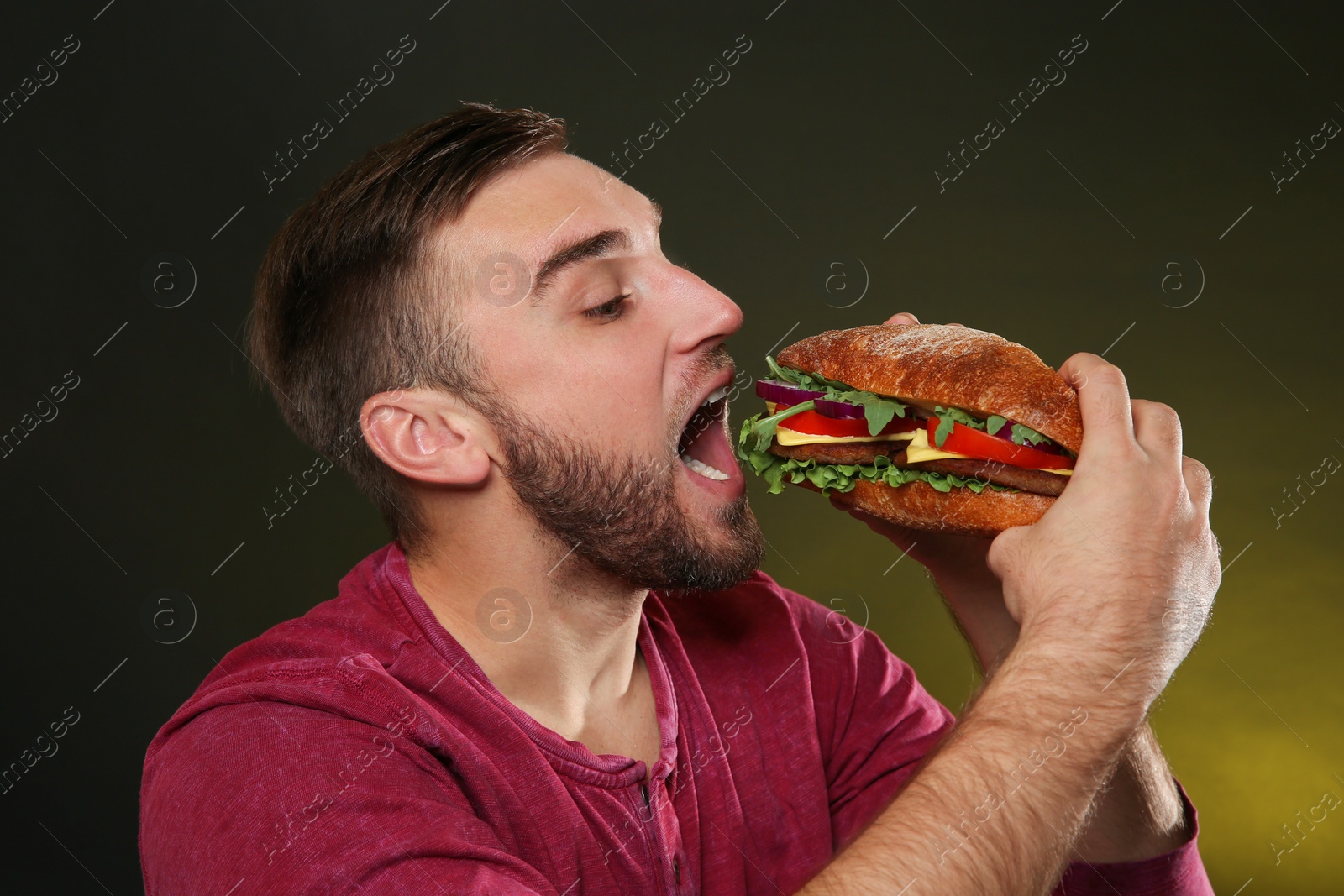 Photo of Young man eating tasty burger on color background