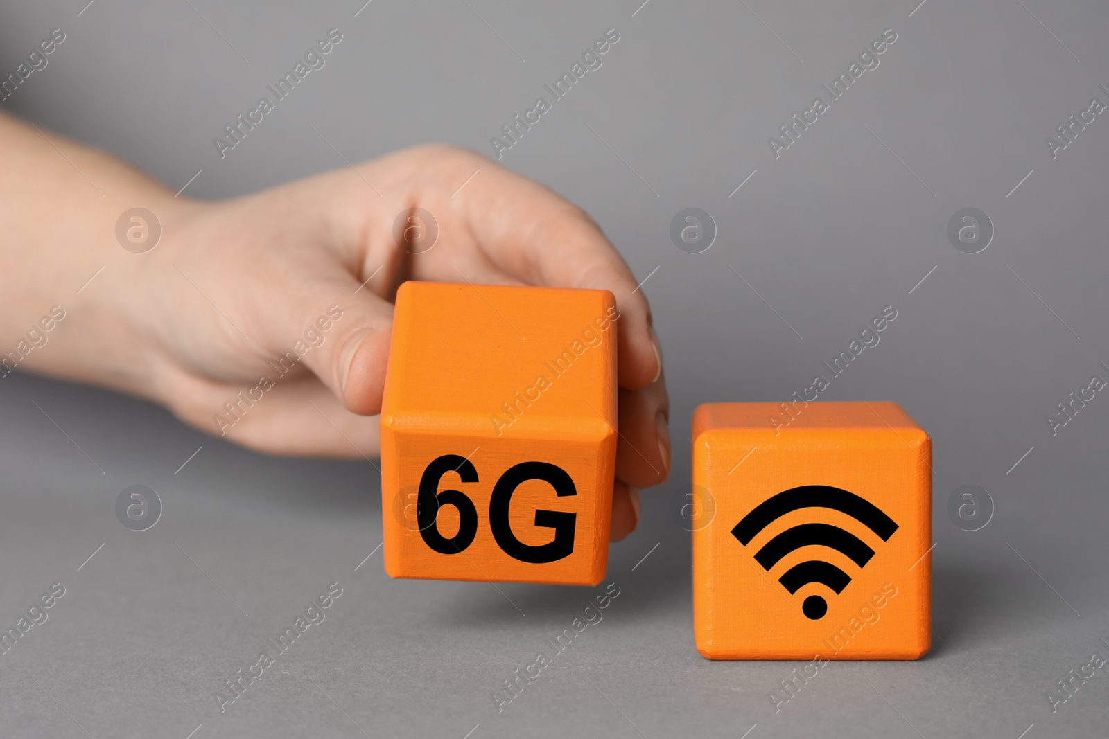 Photo of 6G technology, Internet concept. Woman with orange wooden cubes on grey background, closeup