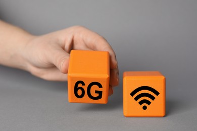 Photo of 6G technology, Internet concept. Woman with orange wooden cubes on grey background, closeup
