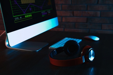 Photo of Modern computer and headphones on table in dark room. Playing video games