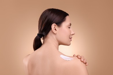 Photo of Beautiful woman with smear of body cream on her shoulder against light brown background, back view