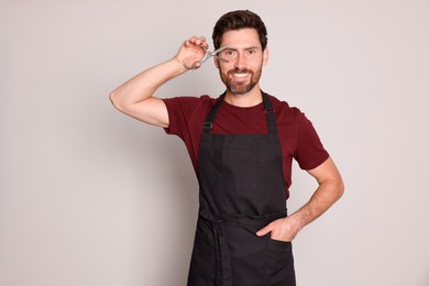 Photo of Smiling hairdresser with scissors on light grey background