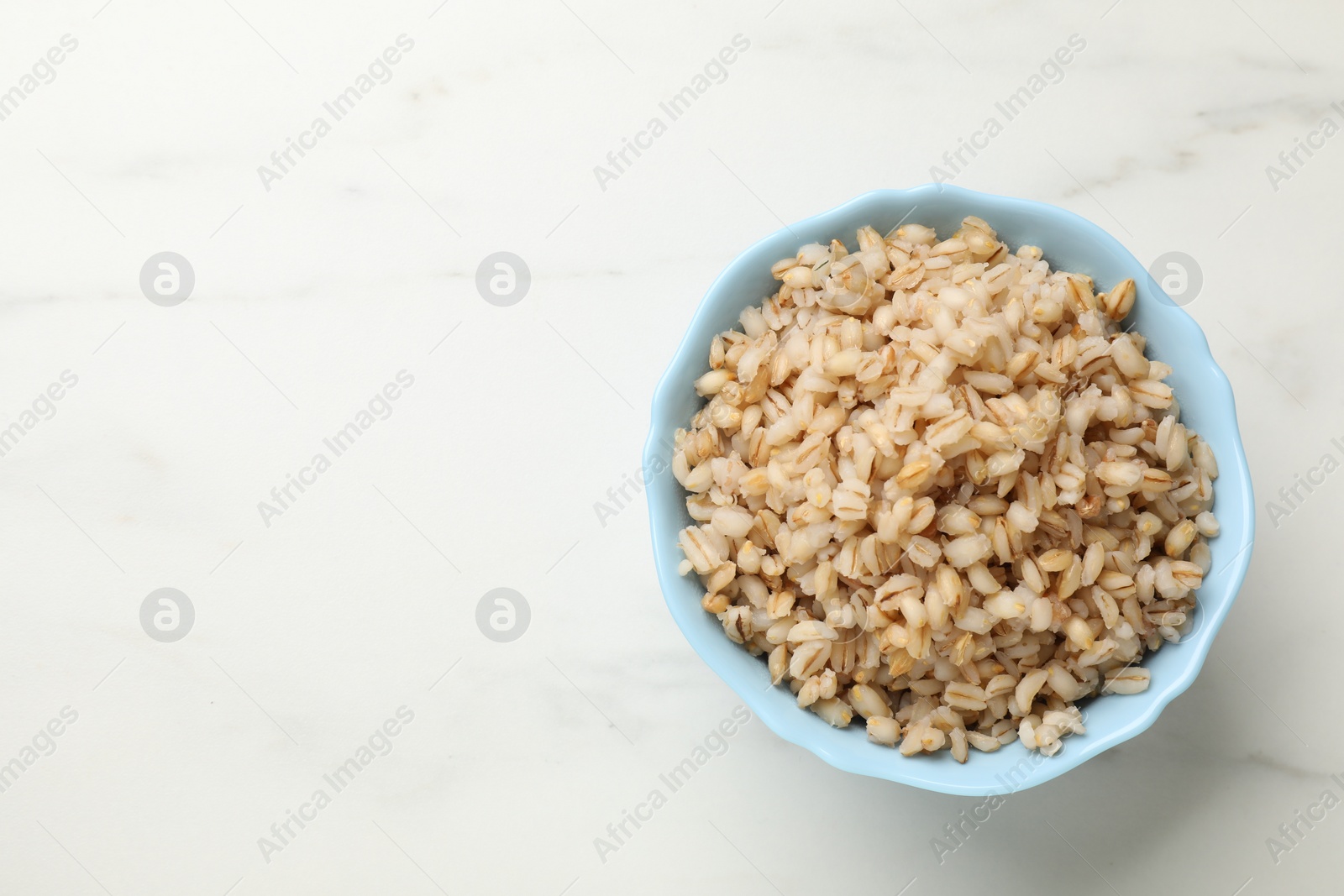 Photo of Delicious pearl barley in bowl on white marble table, top view. Space for text