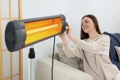 Photo of Woman adjusting temperature on electric infrared heater indoors