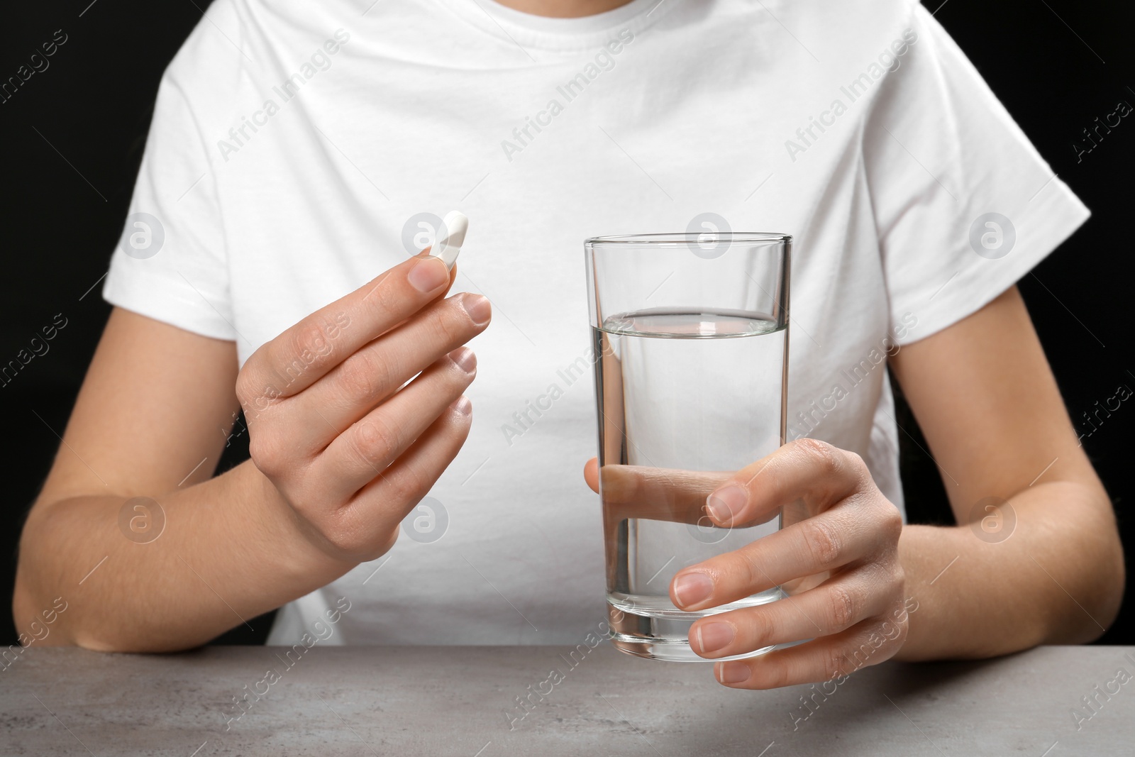 Photo of Woman holding pill and glass of water at table, closeup