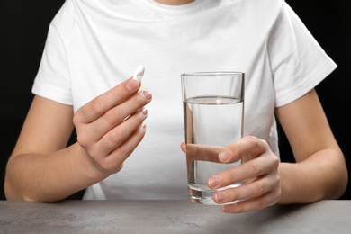 Photo of Woman holding pill and glass of water at table, closeup
