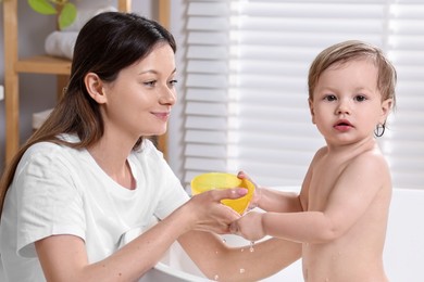 Photo of Mother bathing her cute little baby in tub at home