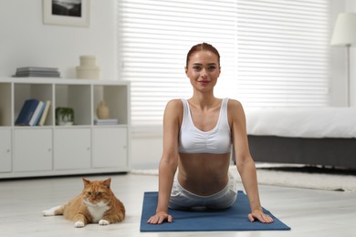 Beautiful woman with cute red cat practicing yoga on mat at home