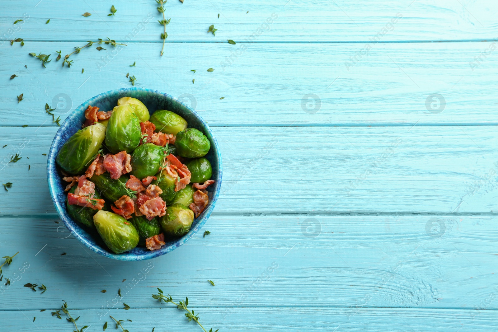 Photo of Tasty roasted Brussels sprouts with bacon on light blue wooden table, flat lay. Space for text