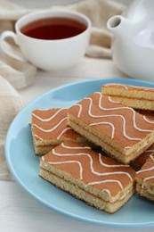 Photo of Tasty sponge cakes and hot drink on while wooden table, closeup