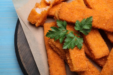Photo of Fresh breaded fish fingers with parsley served on light blue wooden table, top view