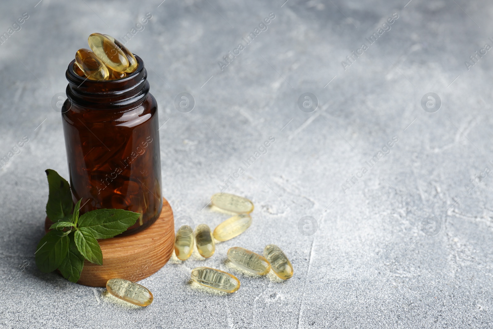 Photo of Medical bottle, mint and yellow capsules on light gray textured table, space for text