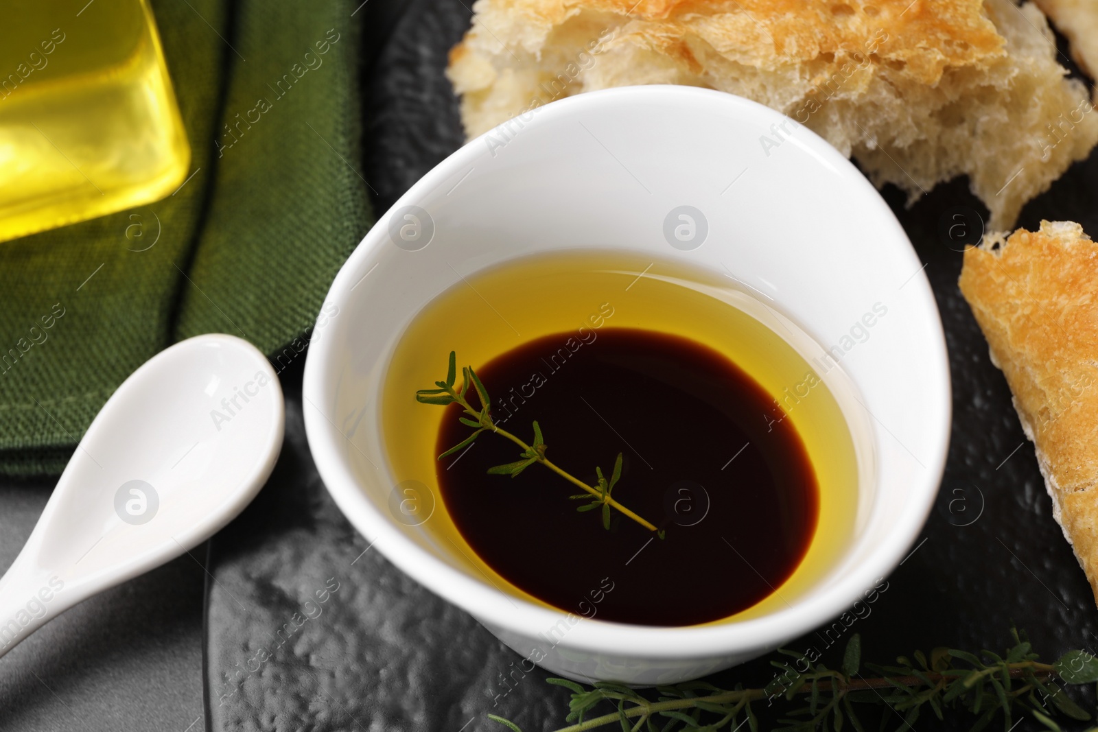 Photo of Bowl of organic balsamic vinegar with oil, thyme and bread on grey table, closeup