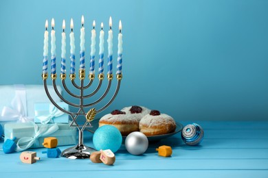Composition with Hanukkah menorah, dreidels, donuts and gift boxes on table against light blue background. Space for text