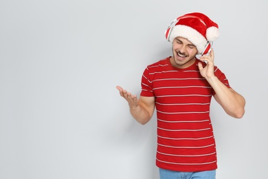 Young man in Santa hat listening to Christmas music on color background