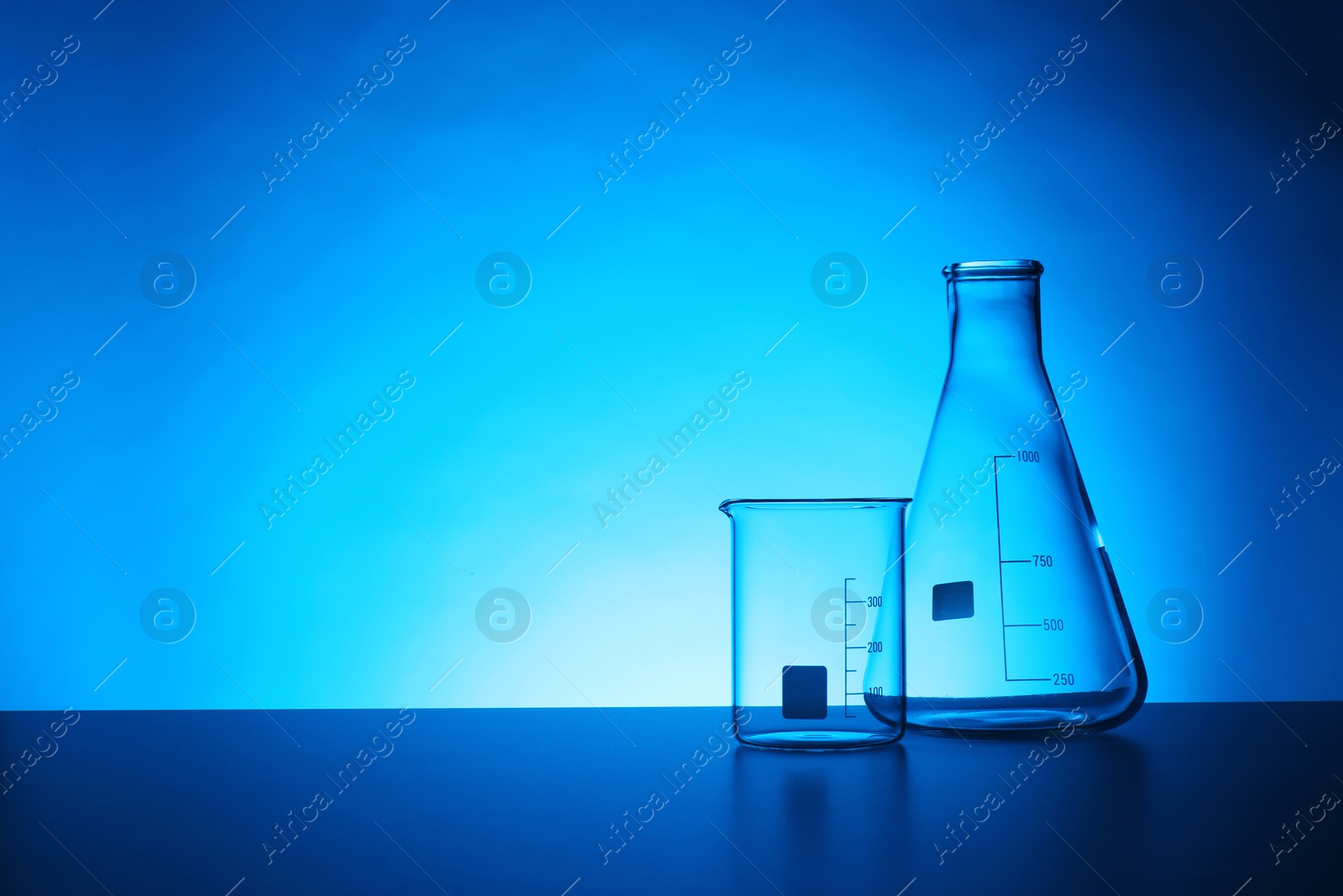 Photo of Empty chemistry laboratory glassware on table against color background