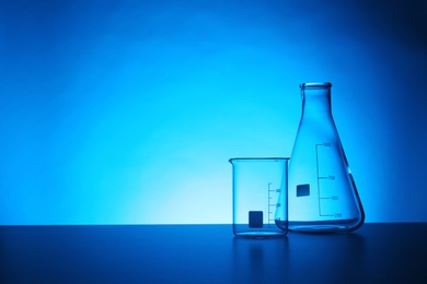 Empty chemistry laboratory glassware on table against color background