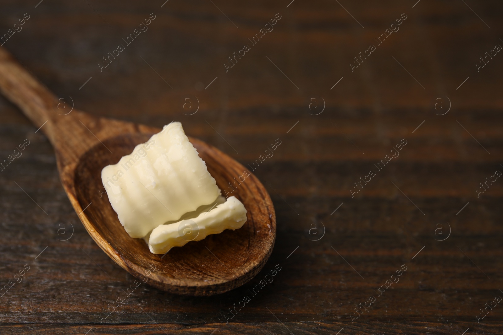 Photo of Tasty butter curl and spoon on wooden table, closeup. Space for text