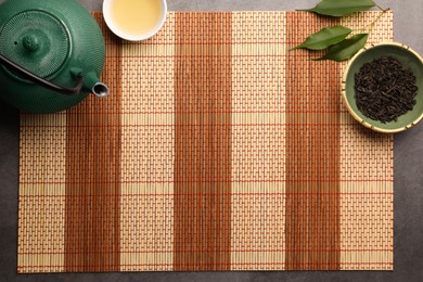 Flat lay composition with bamboo mat, teapot and cup of tea on grey table. Space for text