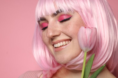 Photo of Smiling woman with bright makeup, fake freckles and tulip on pink background, closeup