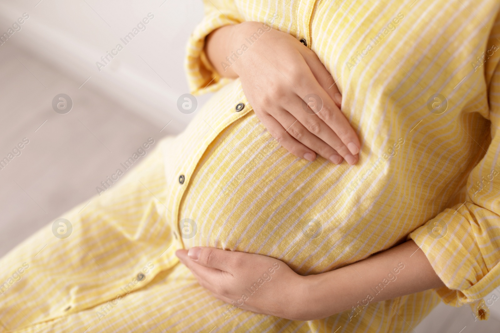 Photo of Beautiful pregnant woman sitting in light room, closeup