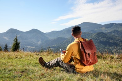 Photo of Tourist with thermos and backpack enjoying beautiful mountain landscape, back view.