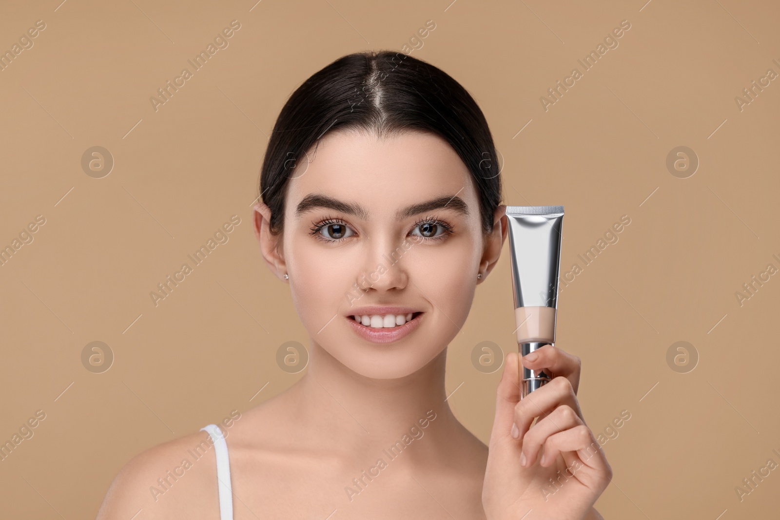 Photo of Teenage girl holding tube with foundation on beige background