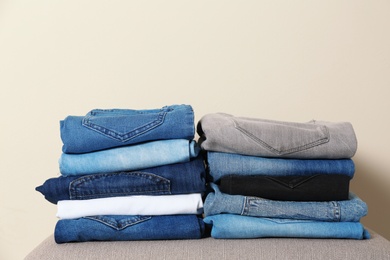 Photo of Stack of different jeans on ottoman against light background