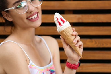 Happy young woman with delicious ice cream in waffle cone near wooden wall, closeup